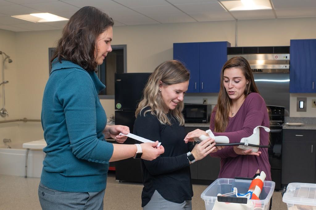 Two U N E 职业治疗 students working with a professor in the O T Lab